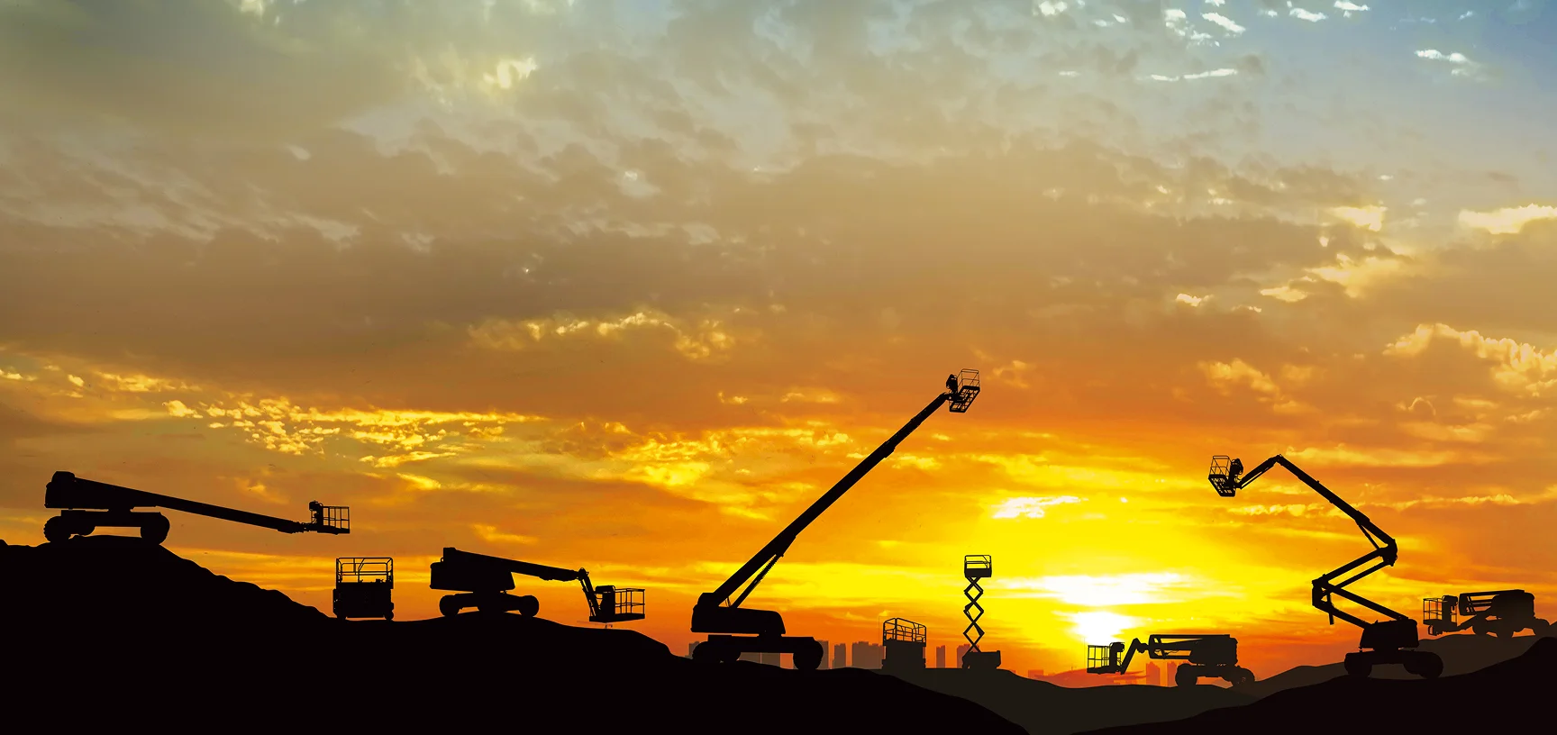 Silhouette of Ant Rentals boom lifts, scissor lifts, and telehandlers against a dramatic orange sunset sky